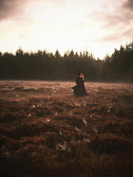 Woman in the misty spider web covered heather holding a candle