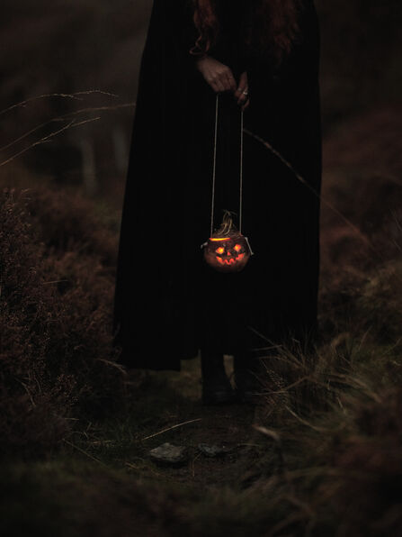 woman in black cloak holding a candle lit turning in the uplands