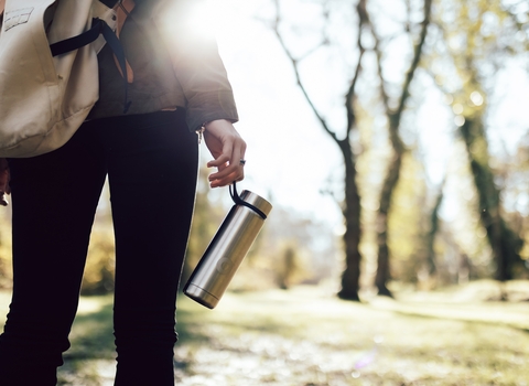 A woman standing outside in the woods with a backpack and water bottle. 